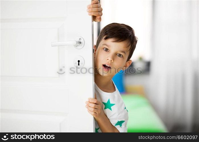 childhood, emotions and people concept - surprised little boy behind door at home. surprised little boy behind door at home