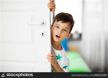 childhood, emotions and people concept - surprised little boy behind door at home. surprised little boy behind door at home