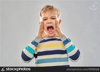 childhood, expressions and people concept - angry little boy in striped pullover screaming over grey background. angry little boy in striped pullover screaming