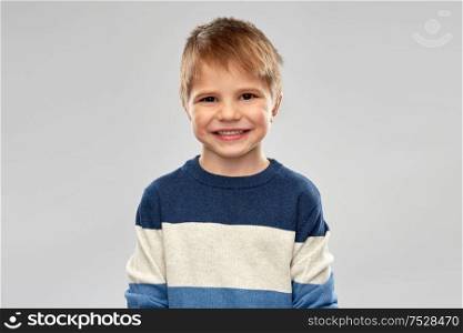 childhood, expressions and people concept - portrait of nice little boy in striped pullover over grey background. portrait of little boy in striped pullover