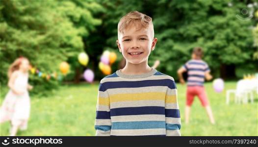 childhood, expressions and people concept - portrait of smiling little boy in striped pullover at birthday party over summer park background. smiling boy at birthday party in summer park