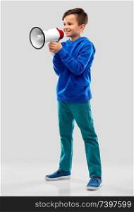 childhood, expressions and people concept - smiling boy in blue hoodie speaking to megaphone over grey background. smiling boy speaking to megaphone
