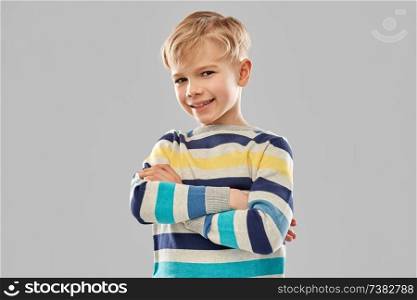 childhood, expressions and people concept - smiling little boy in striped pullover with crossed arms over grey background. smiling boy in striped pullover with crossed arms