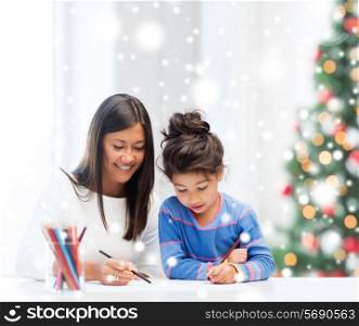 childhood, family, christmas and people concept - smiling little girl and mother or teacher drawing with coloring pencils indoors