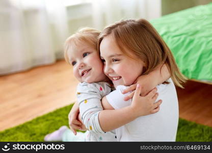 childhood, family, expressions and people concept - happy little girls or sisters hugging at home. happy little girls or sisters hugging at home