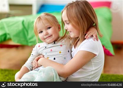 childhood, family, expressions and people concept - happy little girls or sisters hugging at home. happy little girls or sisters hugging at home. happy little girls or sisters hugging at home