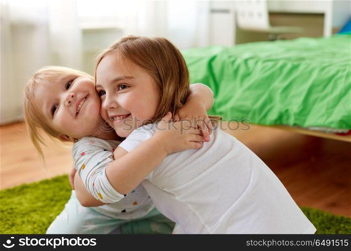 childhood, family, expressions and people concept - happy little girls or sisters hugging at home. happy little girls or sisters hugging at home. happy little girls or sisters hugging at home