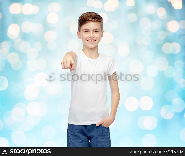 childhood, fashion, advertisement and people concept - happy boy in white t-shirt and jeans pointing finger to you over blue holidays lights background
