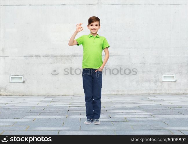 childhood, fashion, advertisement and people concept - happy boy in white t-shirt and jeans showing ok hand sign over urban street background