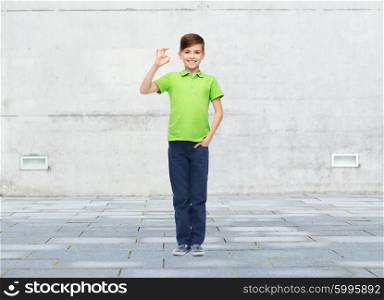 childhood, fashion, advertisement and people concept - happy boy in white t-shirt and jeans showing ok hand sign over urban street background