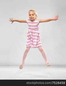 childhood, fashion and people concept - happy little girl in striped dress jumping over grey background. happy little girl in striped dress jumping