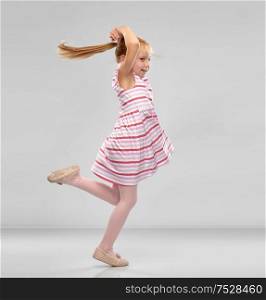 childhood, fashion and people concept - happy little girl in striped dress jumping over grey background. happy little girl in striped dress jumping