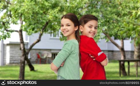 childhood, fashion and people concept - happy smiling boy and girl standing back to back over private house backyard background