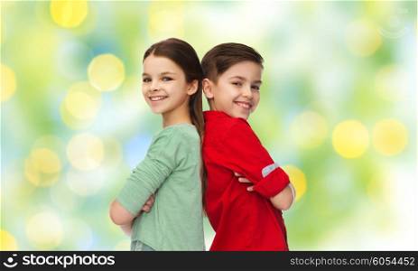 childhood, fashion and people concept - happy smiling boy and girl standing back to back over green lights background