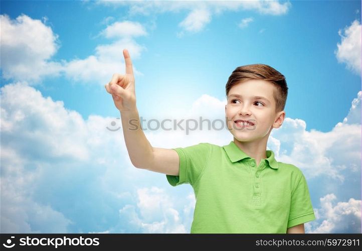 childhood, fashion and people concept - happy smiling boy in green polo t-shirt pointing finger up over blue sky and clouds background
