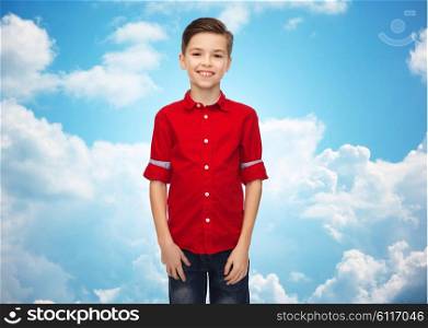 childhood, fashion and people concept - happy smiling boy in red shirt over blue sky and clouds background