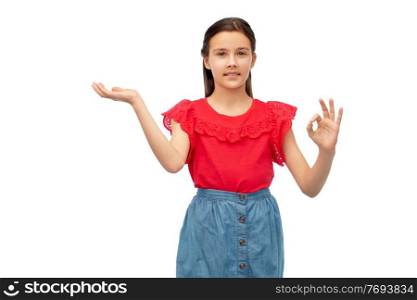 childhood, fashion and people concept - happy smiling girl holding something imaginary on her hand and showing ok sign over white background. girl holding something on hand and showing ok