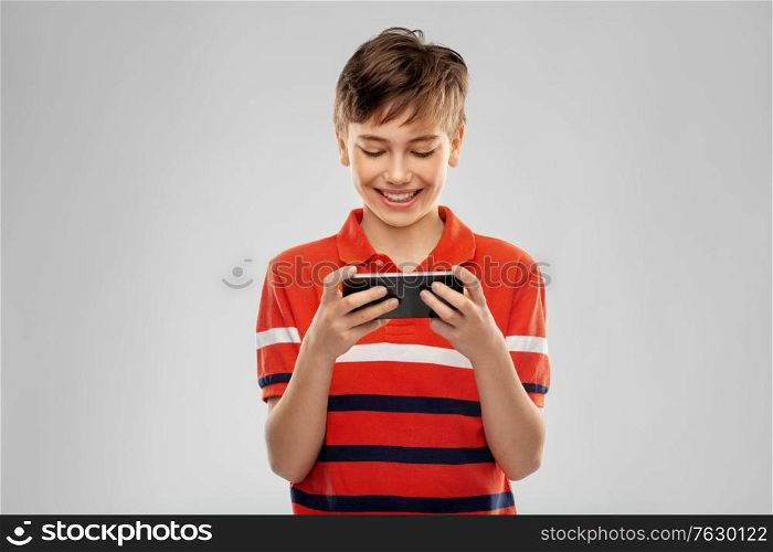 childhood, fashion and people concept - portrait of happy smiling boy in red polo t-shirt with smartphone over grey background. portrait of happy smiling boy with smartphone