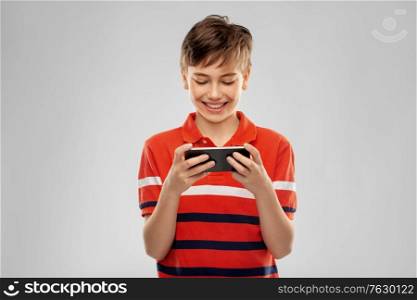 childhood, fashion and people concept - portrait of happy smiling boy in red polo t-shirt with smartphone over grey background. portrait of happy smiling boy with smartphone