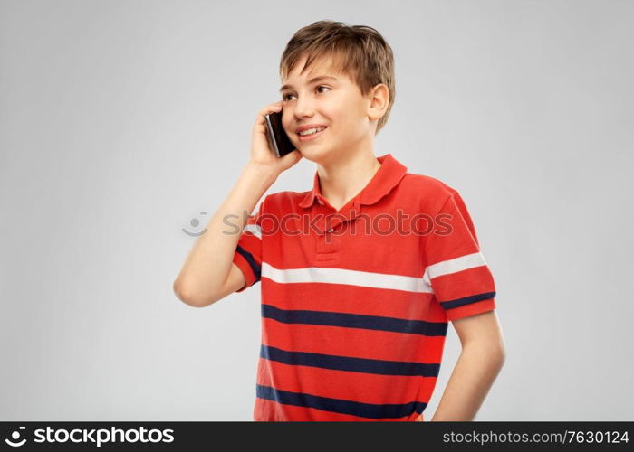 childhood, fashion and people concept - portrait of happy smiling boy in red polo t-shirt calling on smartphone over grey background. happy smiling boy calling on smartphone