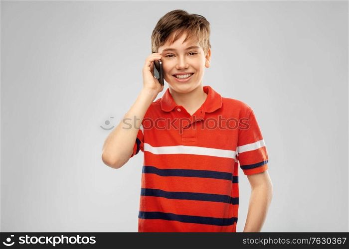 childhood, fashion and people concept - portrait of happy smiling boy in red polo t-shirt calling on smartphone over grey background. happy smiling boy calling on smartphone