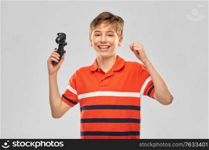 childhood, fashion and people concept - portrait of happy smiling boy in red polo t-shirt with gamepad playing video game over grey background. smiling boy with gamepad playing video game