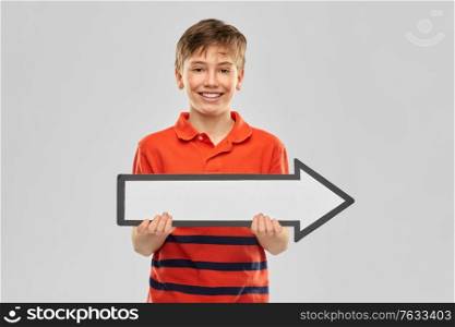 childhood, fashion and people concept - portrait of happy smiling boy in red polo t-shirt holding big white rightwards thick arrow over grey background on grey background. happy boy holding big white rightwards thick arrow