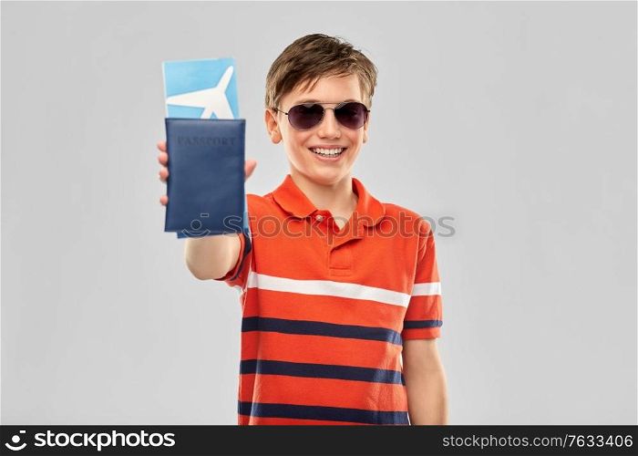 childhood, fashion and people concept - portrait of happy smiling boy in sunglasses and red polo t-shirt with air ticket and passport over grey background. happy boy in sunglasses with ticket and passport
