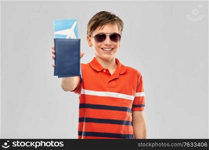 childhood, fashion and people concept - portrait of happy smiling boy in sunglasses and red polo t-shirt with air ticket and passport over grey background. happy boy in sunglasses with ticket and passport