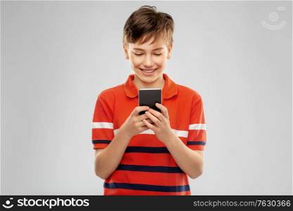 childhood, fashion and people concept - portrait of happy smiling boy with smartphone in red polo t-shirt over grey background. portrait of happy smiling boy with smartphone