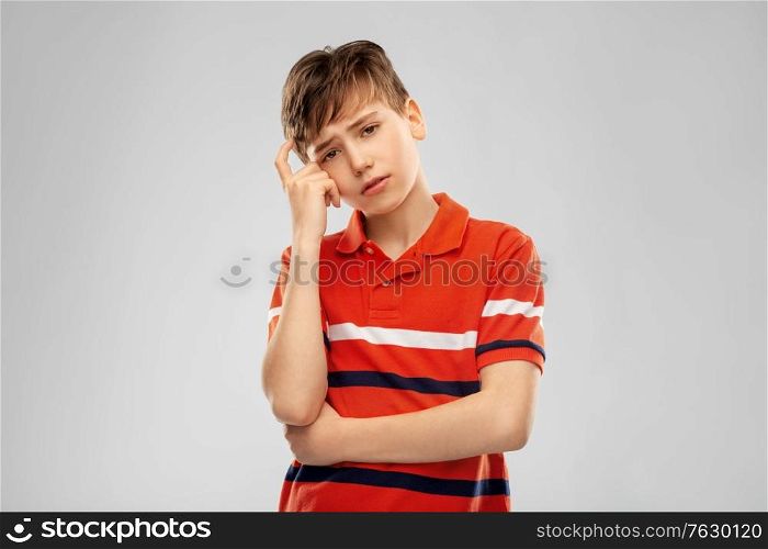 childhood, fashion and people concept - portrait of sad thinking boy in red polo t-shirt over grey background. portrait of sad thinking boy in red polo t-shirt