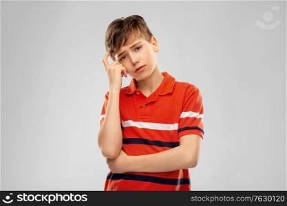 childhood, fashion and people concept - portrait of sad thinking boy in red polo t-shirt over grey background. portrait of sad thinking boy in red polo t-shirt