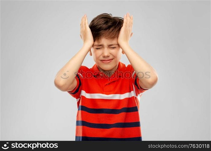 childhood, fashion and people concept - portrait of stressed boy in red polo t-shirt having headache over grey background. stressed boy in red polo t-shirt having headache