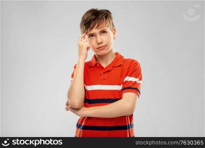 childhood, fashion and people concept - portrait of thinking boy in red polo t-shirt over grey background. portrait of thinking boy in red polo t-shirt