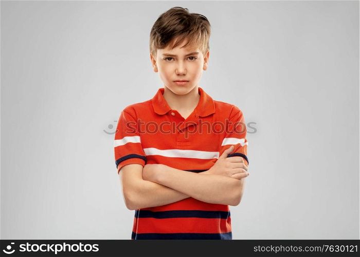 childhood, fashion and people concept - portrait of unhappy boy in red polo t-shirt with crossed arms over grey background. portrait of unhappy boy in red polo t-shirt