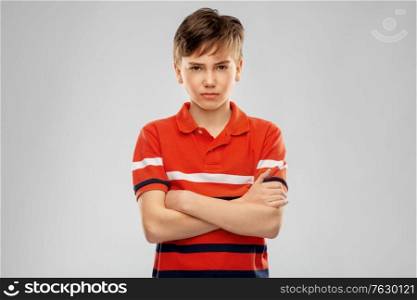 childhood, fashion and people concept - portrait of unhappy boy in red polo t-shirt with crossed arms over grey background. portrait of unhappy boy in red polo t-shirt