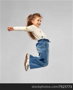 childhood, fashion and people concept - smiling little girl in jeans jumping over grey background. smiling little girl jumping