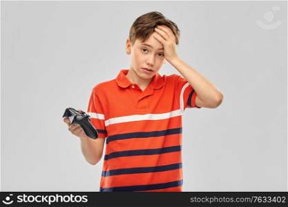 childhood, fashion and people concept - unhappy boy in red polo t-shirt with gamepad playing video game over grey background. unhappy boy with gamepad playing video game