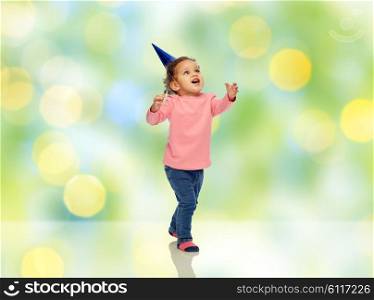 childhood, fashion, birthday, holidays and people concept - happy smiling african american little baby girl with birthday party hat catching something over green summer holidays lights background
