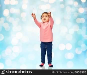 childhood, fashion, clothing and people concept - beautiful little african american baby girl playing with soap bubble over blue holidays lights background