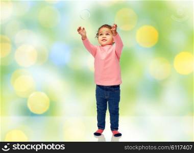 childhood, fashion, clothing and people concept - beautiful little african american baby girl playing with soap bubble over green summer light background