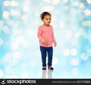 childhood, fashion, clothing and people concept - beautiful little african american baby girl walking over blue holidays lights background