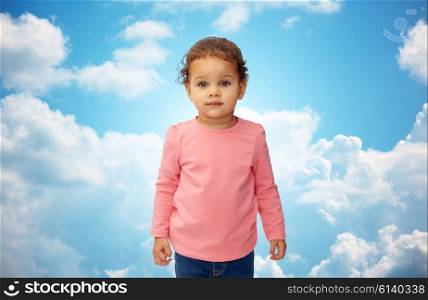 childhood, fashion, clothing and people concept - beautiful little african american baby girl portrait over blue sky and clouds background