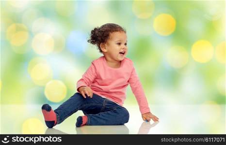 childhood, fashion, clothing and people concept - smiling beautiful african american little baby girl sitting on floor over green summer light background