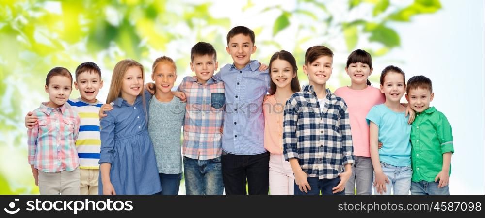 childhood, fashion, friendship and people concept - group of happy smiling children hugging over green natural background