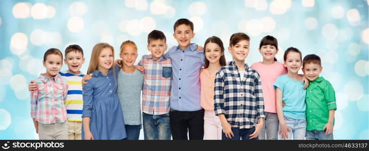 childhood, fashion, friendship and people concept - group of happy smiling children hugging over blue holidays lights background