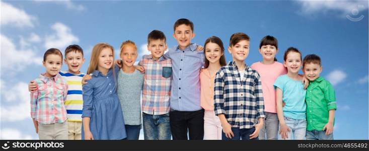childhood, fashion, friendship and people concept - group of happy smiling children hugging over blue sky and clouds background