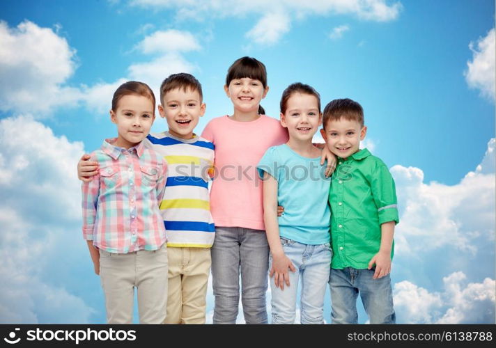 childhood, fashion, friendship and people concept - group of happy smiling little children hugging over blue sky and clouds background