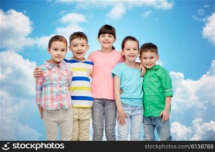 childhood, fashion, friendship and people concept - group of happy smiling little children hugging over blue sky and clouds background