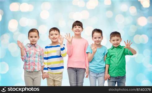 childhood, fashion, friendship and people concept - group of happy smiling little children holding hands over blue holidays lights background